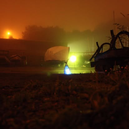 Atmospheric nighttime photograph in orange fog with a bright green light and bicycle silhouette.